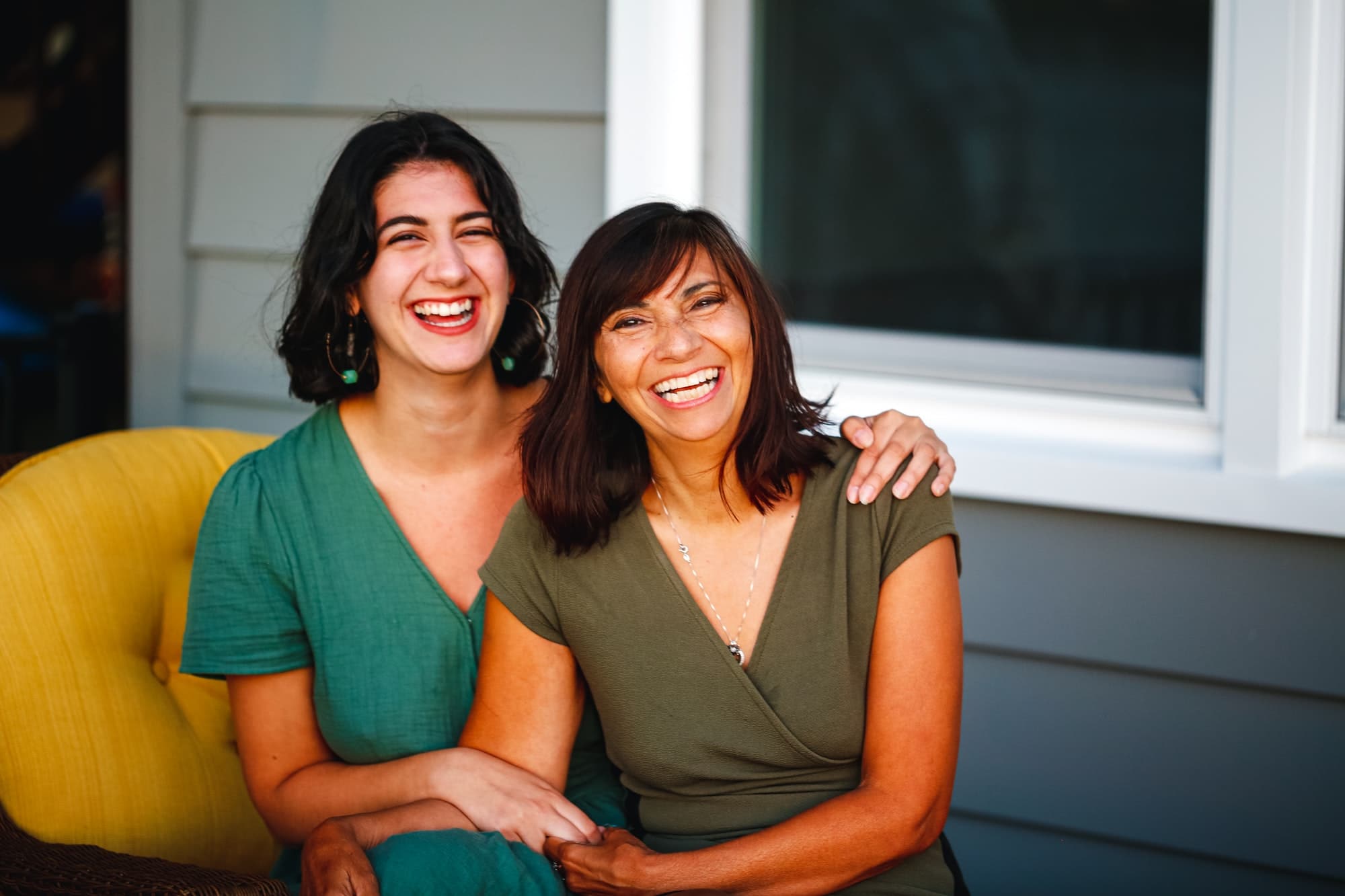Smiling and laughing beautiful Latina mom and biracial millennial daughter family portrait